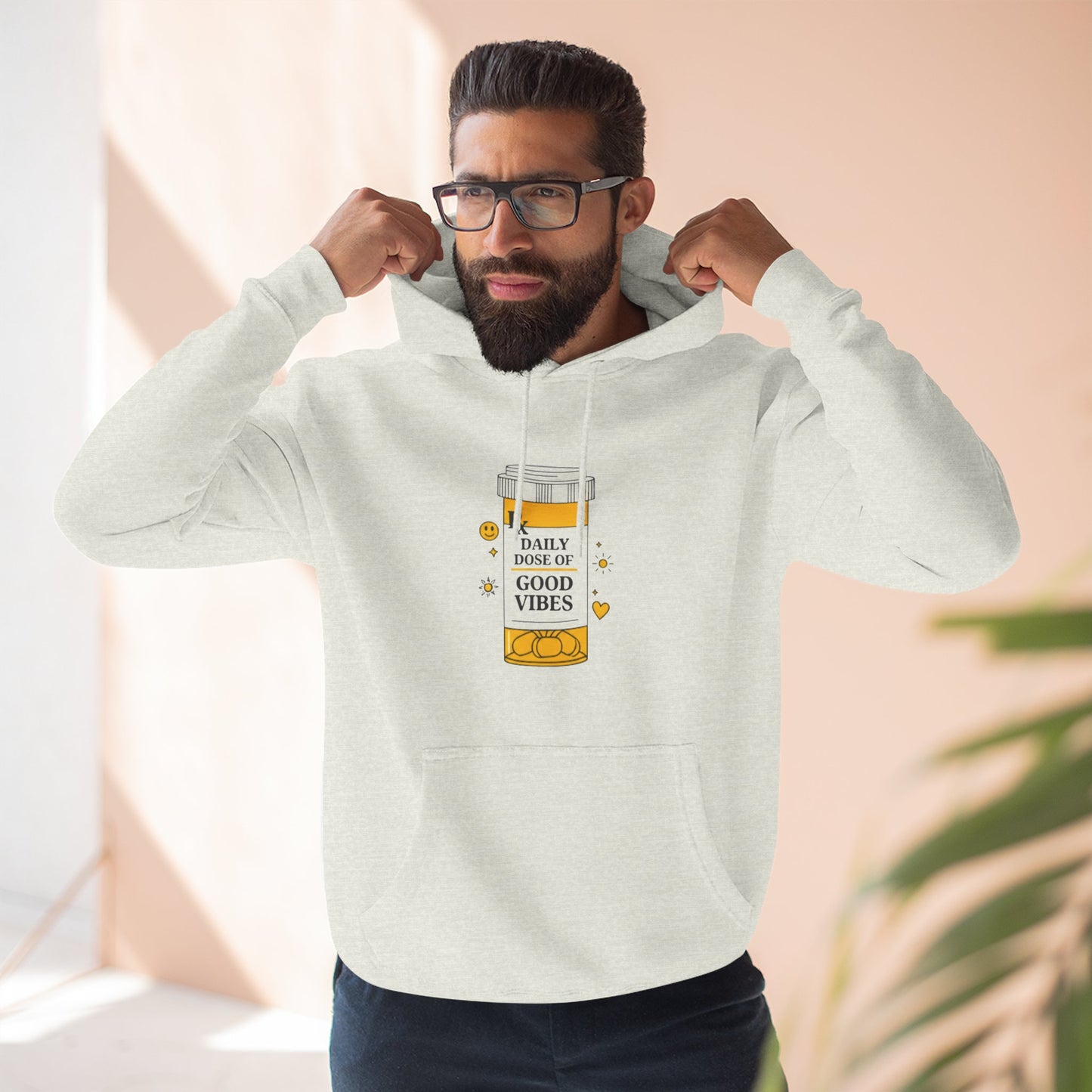 Man wearing a light beige hoodie with a daily dose of good vibes design on a neutral background