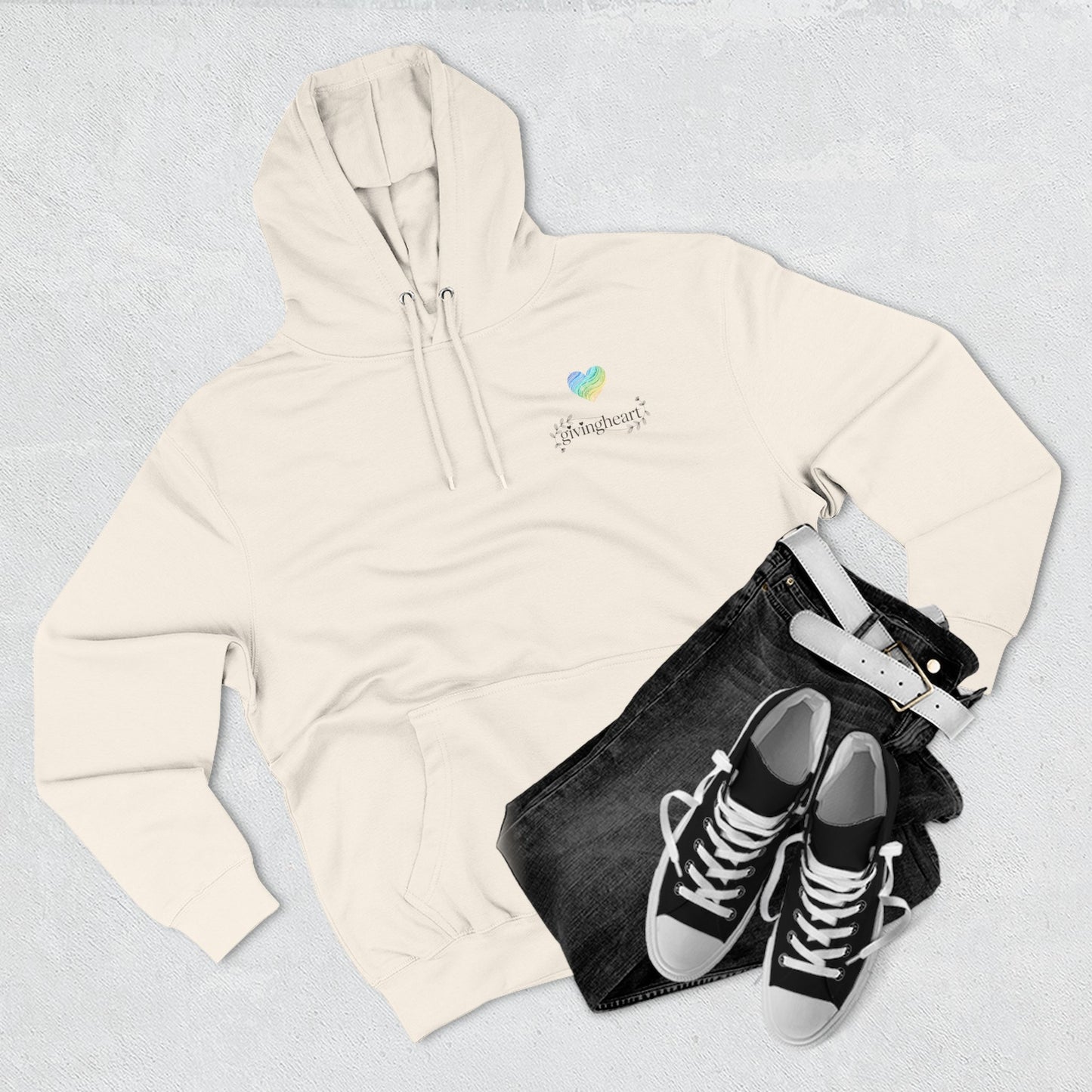 Beige hoodie with a blue/green/yellow heart logo logo, black jeans, and black sneakers on a light gray background