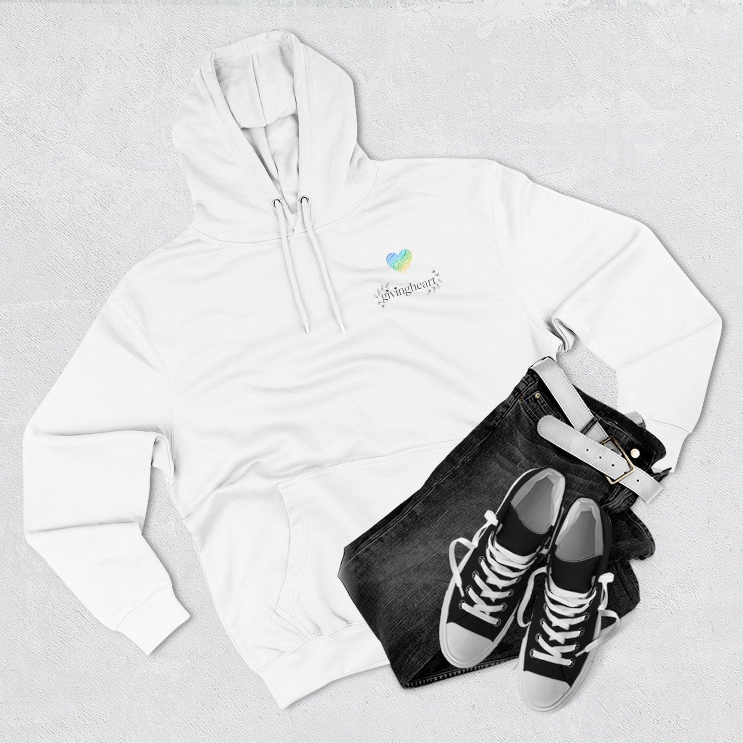 White hoodie with a blue/green/yellow heart logo logo, black jeans, and black sneakers on a light gray background