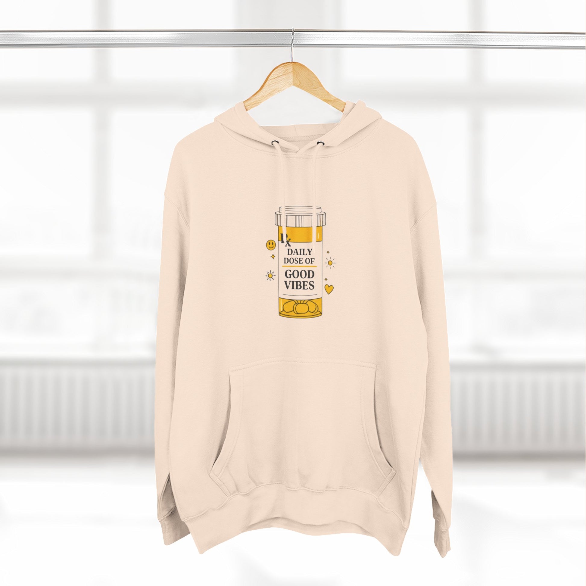 Pale pink hoodie with a daily dose of good vibes design  design on a hanger against a white background