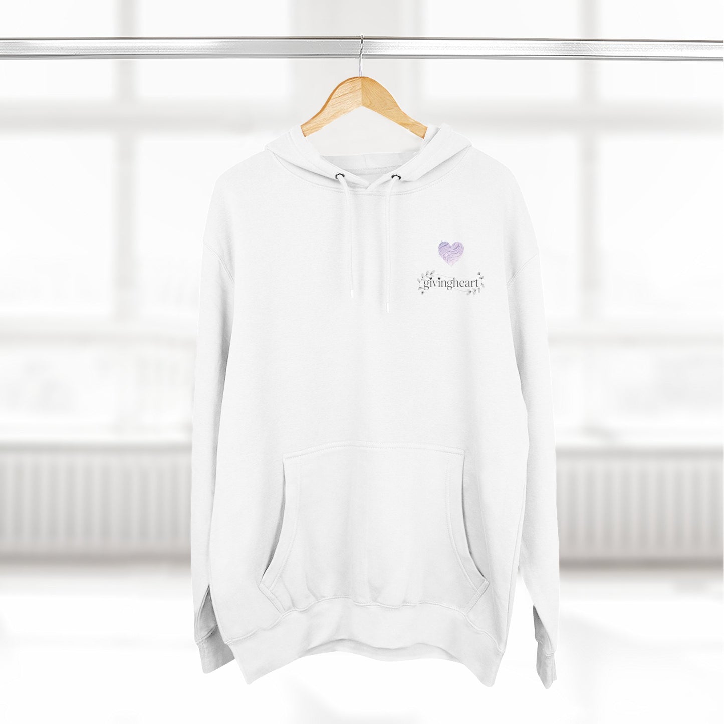 White hoodie with a lilac colored heart logo on a wooden hanger against a white background