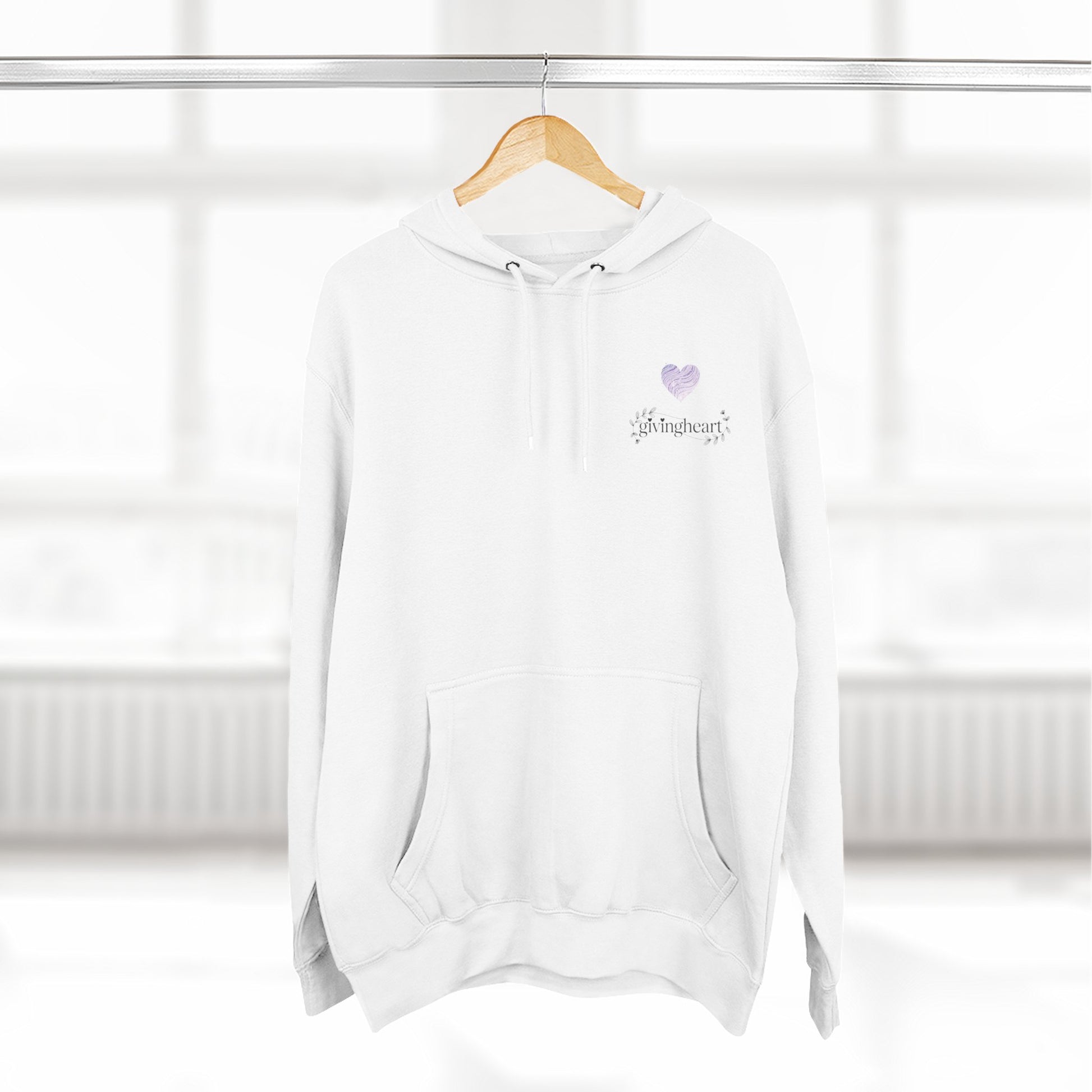 White hoodie with a lilac colored heart logo on a wooden hanger against a white background