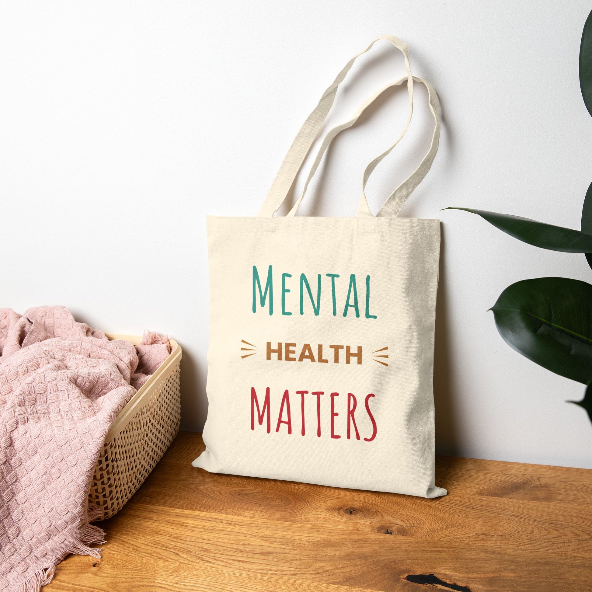 Tote bag with 'Mental Health Matters' text on a wooden surface with a plant in the background