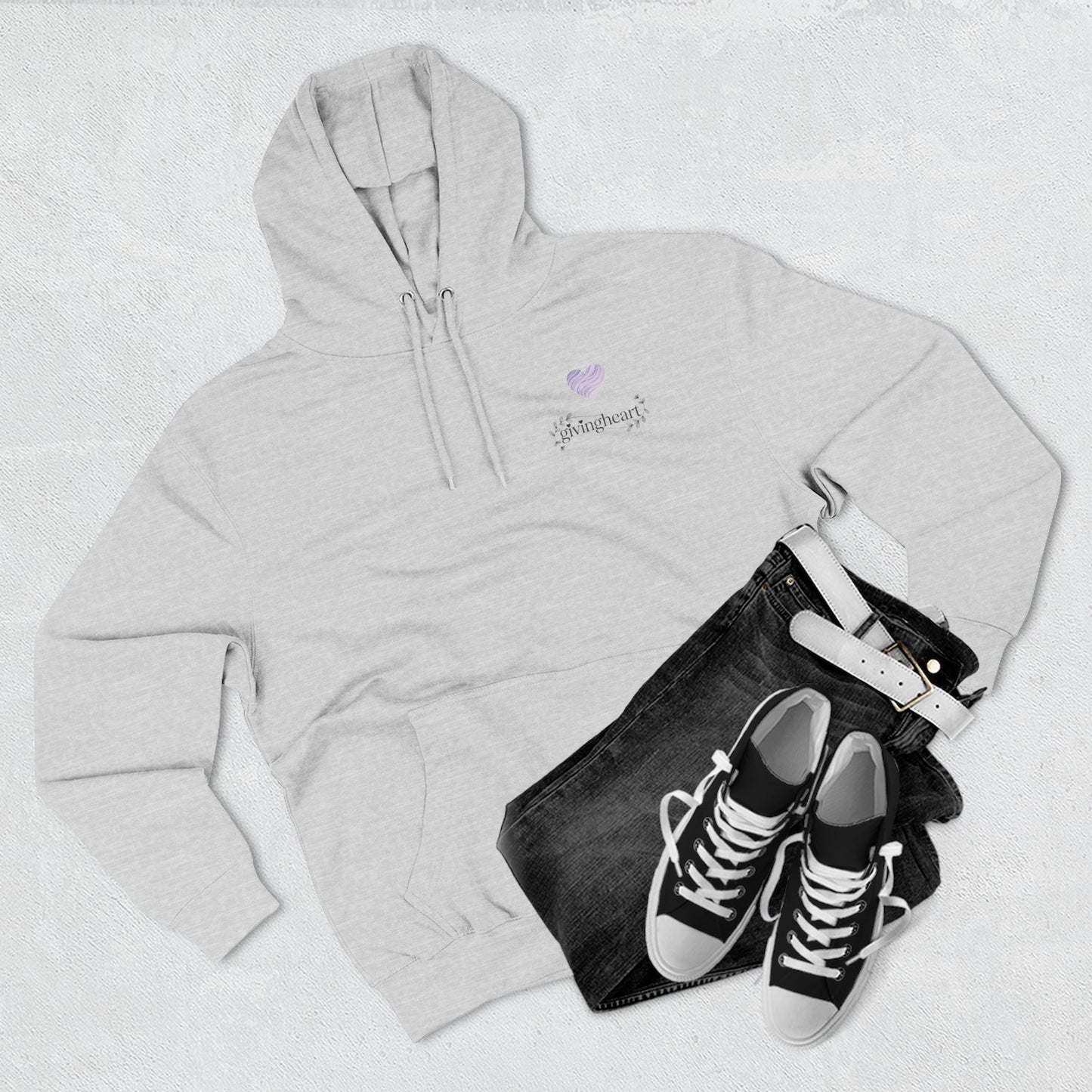 Gray hoodie with a lilac colored heart logo, black jeans, and black sneakers on a light gray background