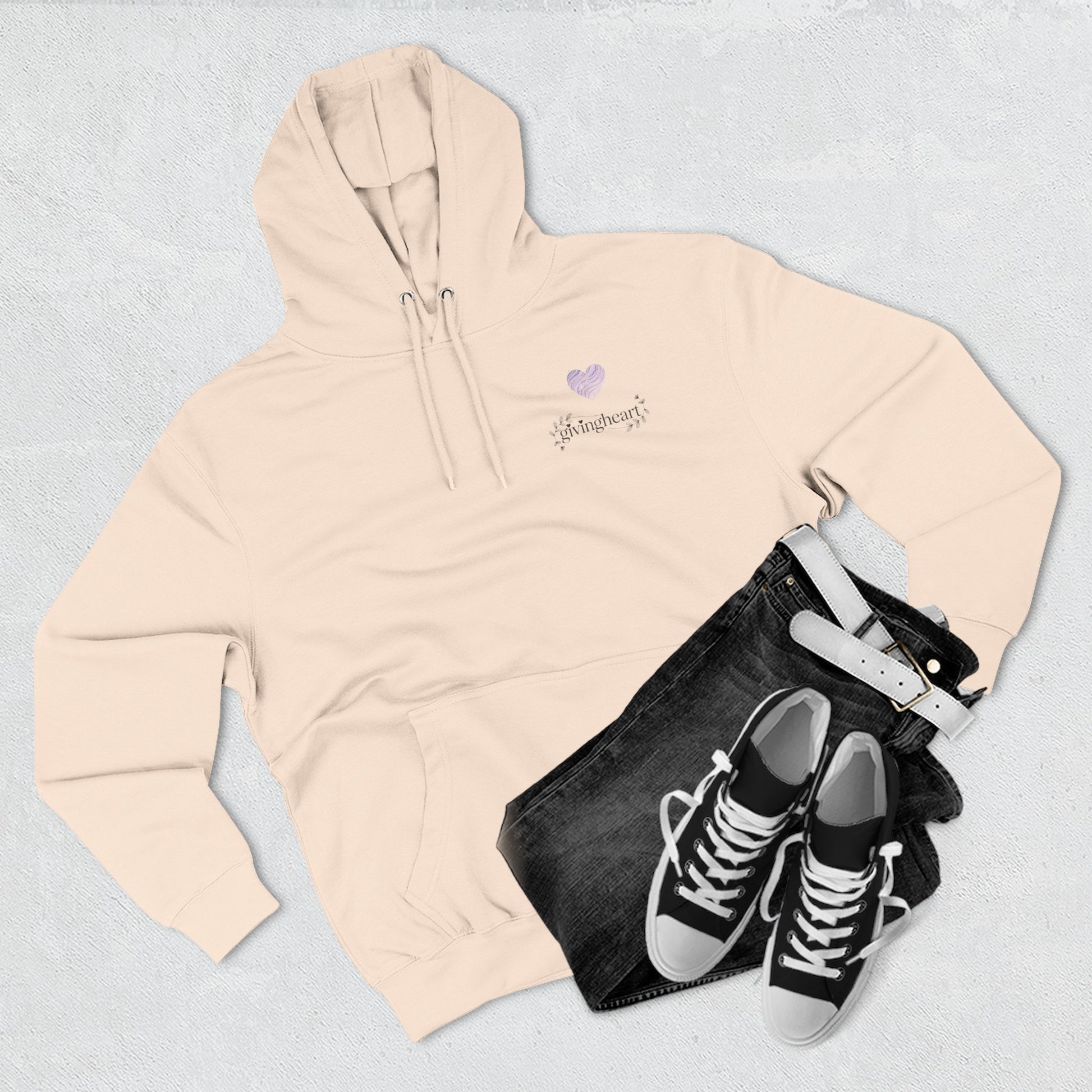 Beige hoodie with a lilac colored heart logo, black jeans, and black high-top sneakers on a light gray background