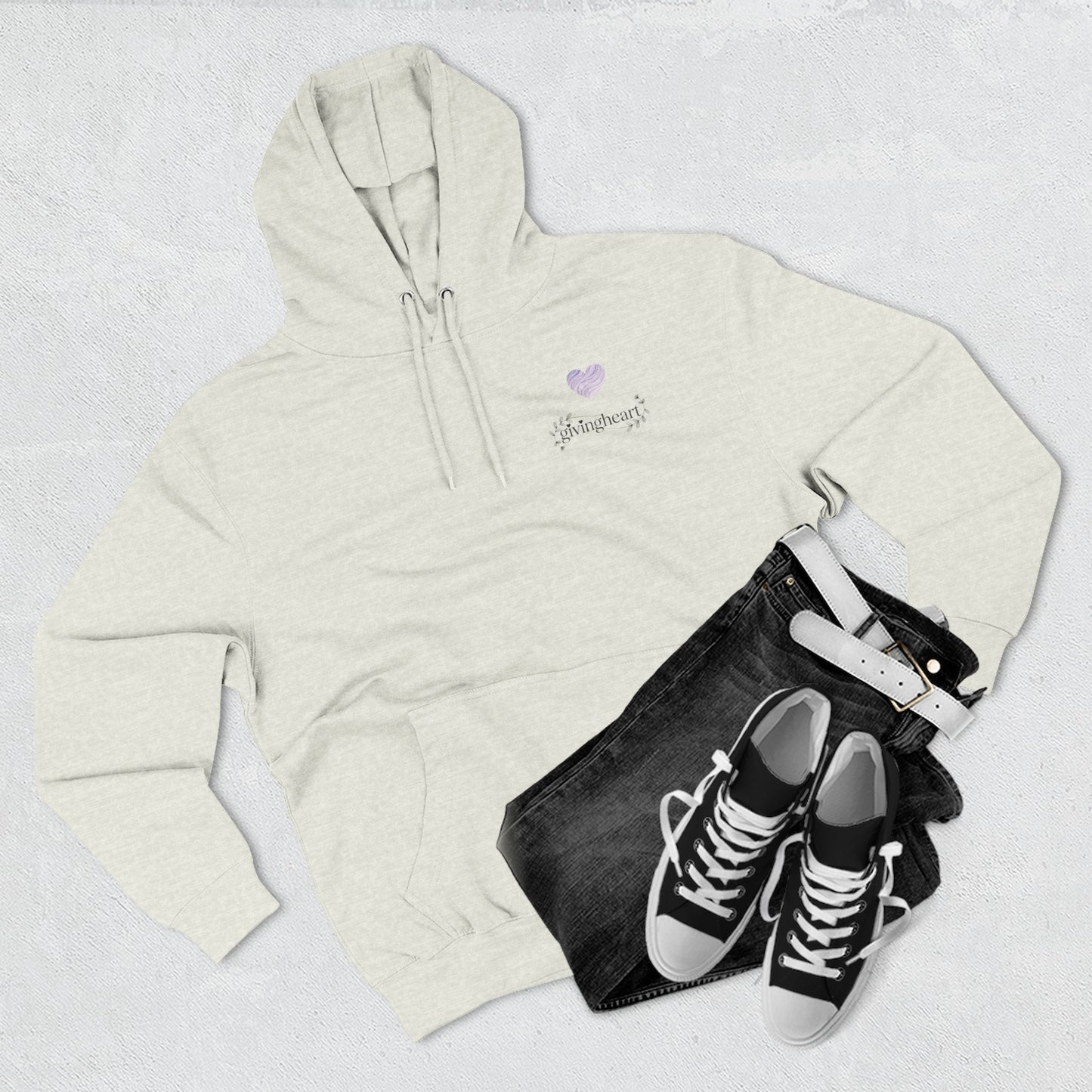 Beige hoodie with a lilac colored heart logo, black jeans, and black sneakers on a light gray background