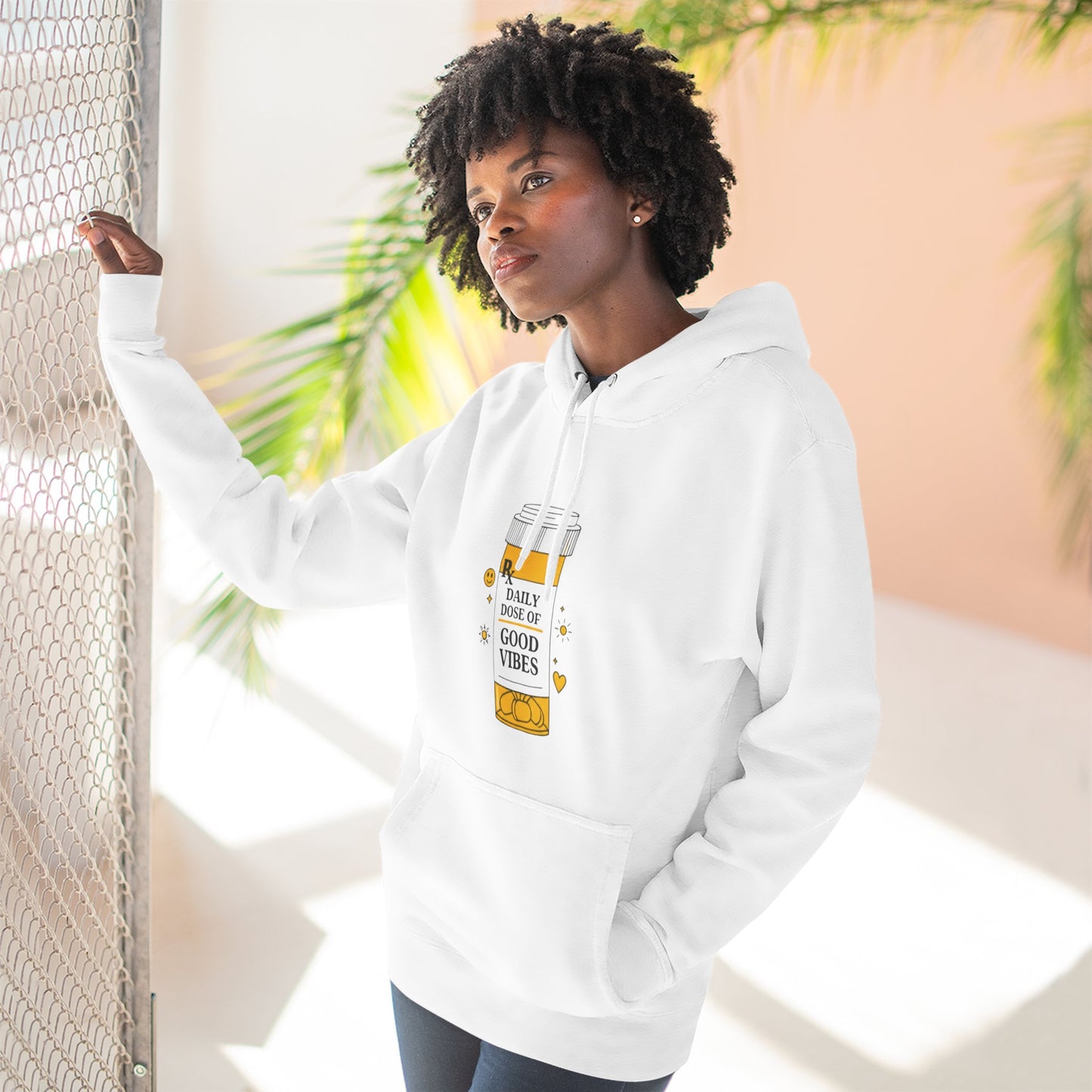 Person wearing a white hoodie with a daily dose of good vibes design , standing indoors with plants in the background