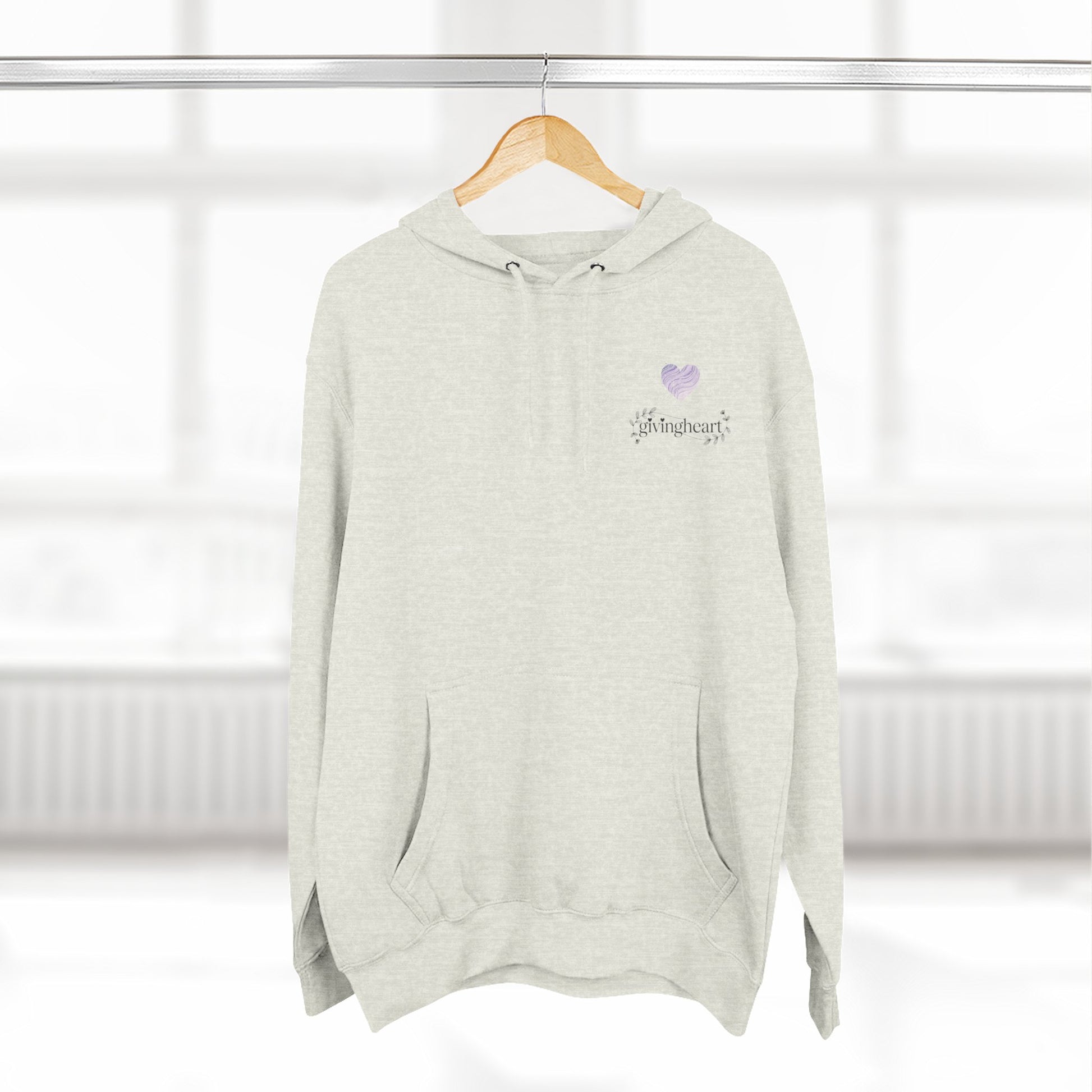 Light gray hoodie with a lilac colored heart logo on a wooden hanger against a white background